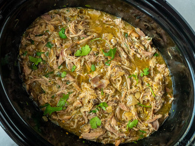Slow cooker filled with pork simmering in chile verde sauce made with Spicito Chile Verde Bombs.