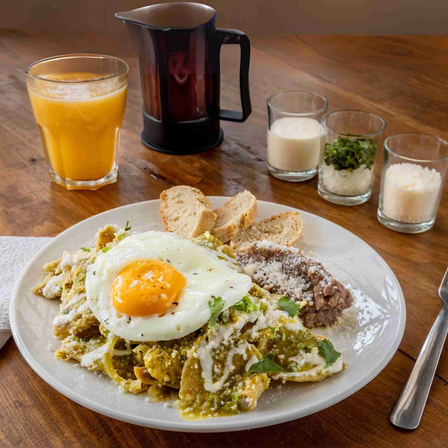 Breakfast plate with eggs, greens, and bread on a wooden table with glasses of orange juice and milk.