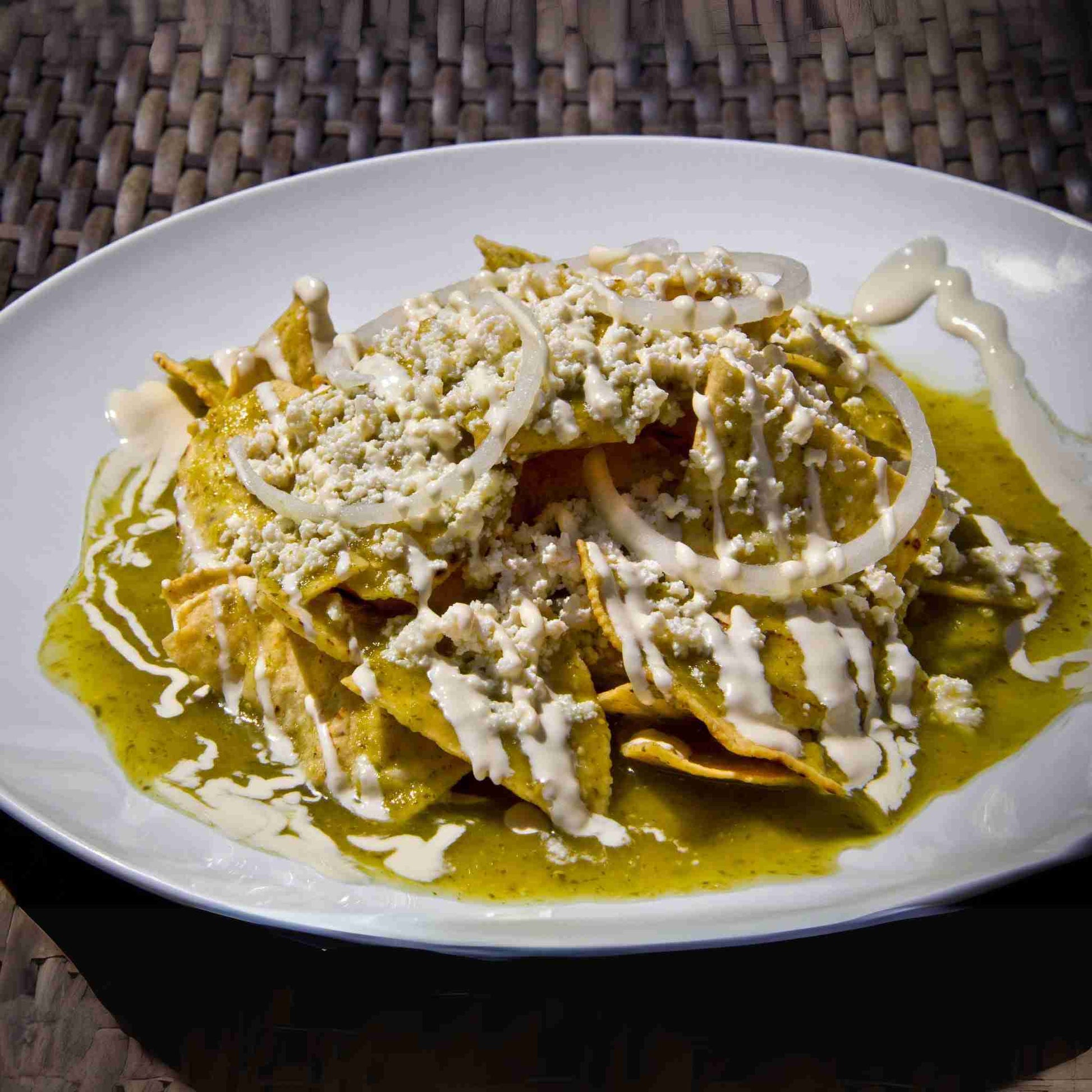 Plated dish of chilaquiles with green sauce, cheese, and onions on a white plate.